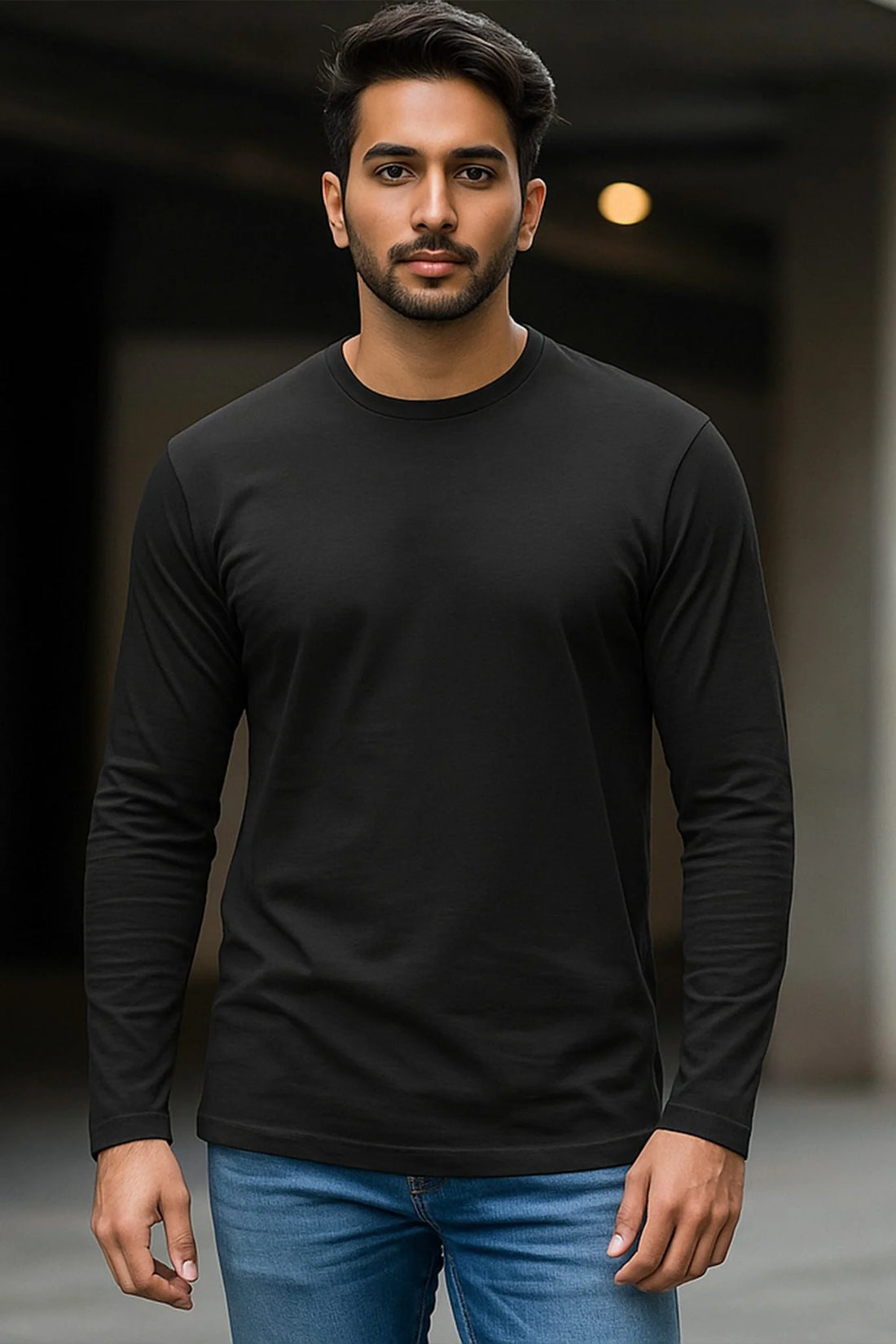 Man wearing a black long-sleeve shirt and blue jeans against a blurred background