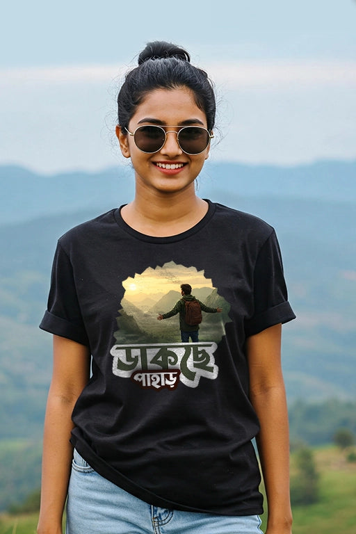 Person wearing a black t-shirt with a graphic design and text, standing in front of a scenic mountain background.