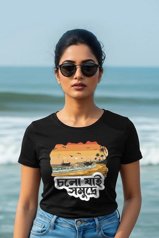 Woman wearing a black t-shirt with a graphic design and text, standing on a beach.