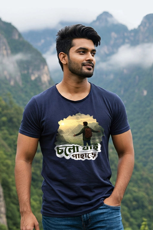 Man wearing a navy blue t-shirt with a graphic design and text, standing against a mountainous background.