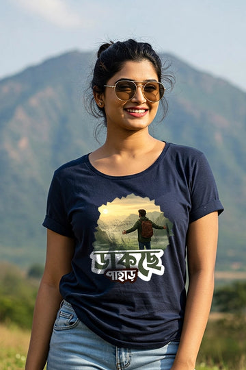 Woman wearing a navy blue t-shirt with a graphic design and text, standing in front of a mountainous landscape.