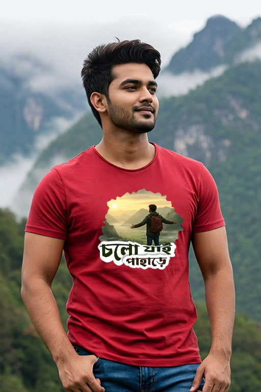 Man wearing a red t-shirt with a mountain graphic and text, standing in front of a scenic background.