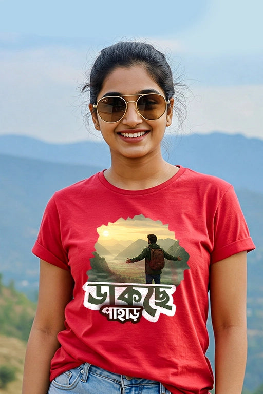 Person wearing a red t-shirt with a graphic design and text, standing outdoors with mountains in the background.