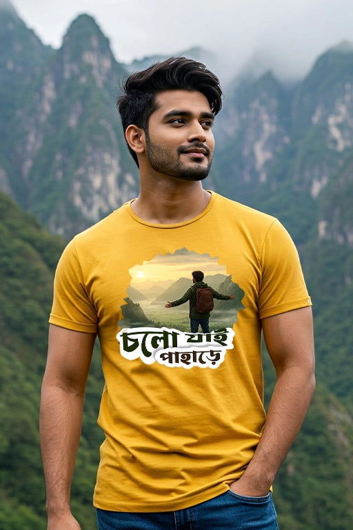 Man wearing a yellow t-shirt with a graphic design and text, standing against a mountainous background.