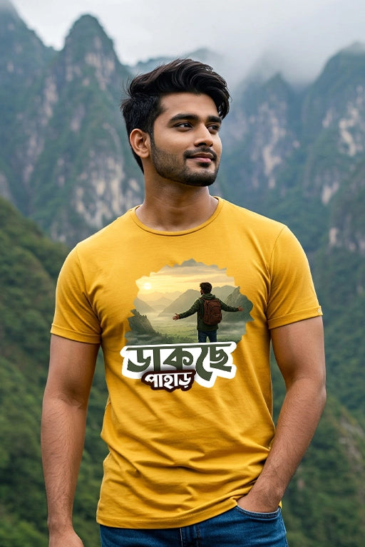 Man wearing a yellow t-shirt with a graphic design of a person in nature, standing against a mountainous background.
